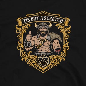 May include: Black t-shirt with a graphic of a Viking giving a thumbs up, with the text "Tis but a scratch." The design is framed in gold with a D20 die. The Dungeon Arsenal logo is at the bottom.