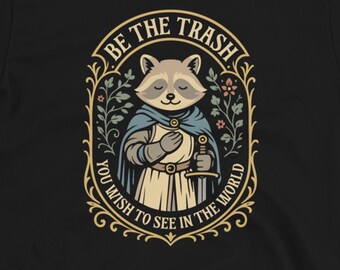 May include: Black t-shirt featuring a cartoon raccoon dressed as a knight, holding a sword. The design is framed by an oval with the text "BE THE TRASH YOU WISH TO SEE IN THE WORLD". The Dungeon Arsenal logo is at the bottom.
