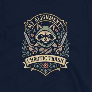 May include: Navy blue t-shirt featuring a raccoon character with two knives, wearing a hood, and the text "My Alignment? Chaotic Trash." The design is framed with floral elements.
