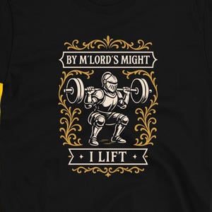 May include: Black t-shirt featuring a weightlifting knight graphic. The design includes the text "BY M'LORD'S MIGHT" above the knight and "I LIFT" below. The shirt has a crew neck and short sleeves.