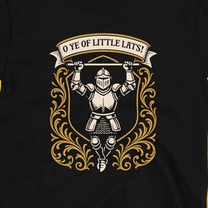 May include: Black t-shirt with a medieval knight graphic. The knight is holding a banner that reads "O YE OF LITTLE LATS!" The design is framed by an ornate gold border. The Dungeon Arsenal logo is at the bottom.