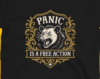 May include: Black t-shirt with a graphic featuring a snarling opossum inside a decorative frame. The text reads "PANIC IS A FREE ACTION" in a vintage style. The shirt is displayed against a yellow background with skull patterns.