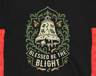 May include: Black t-shirt featuring a bell design with the text "Blessed be the Blight." The bell is cream-colored with green and brown accents, surrounded by a decorative floral border. The shirt is a classic crew neck.