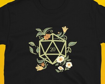 Puede incluir: Camiseta negra con un diseño floral verde, blanco y naranja con un dado de 20 caras en el centro. El texto "Dungeon Arsenal" está impreso en la parte inferior de la imagen.