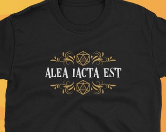 Könnte beinhalten: Schwarzes T-Shirt mit dem lateinischen Satz "ALEA IACTA EST" in Weiß, umrahmt von goldenen dekorativen Elementen und Würfelformen. Das Shirt stammt von Dungeon Arsenal, einer Marke, die sich auf Gaming-Bekleidung spezialisiert hat.