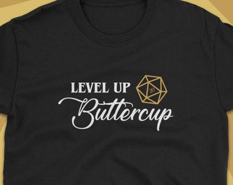 Könnte beinhalten: Schwarzes T-Shirt mit weißem Text "Level Up Buttercup" und einer goldenen 20-seitigen Würfelgrafik.