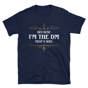 K&ouml;nnte beinhalten: Marineblaues T-Shirt mit dem wei&szlig;en Text "BECAUSE I'M THE DM THAT'S WHY." und goldenen Verzierungen. Das Shirt mit Rundhalsausschnitt und kurzen &Auml;rmeln ist f&uuml;r Rollenspiele geeignet.