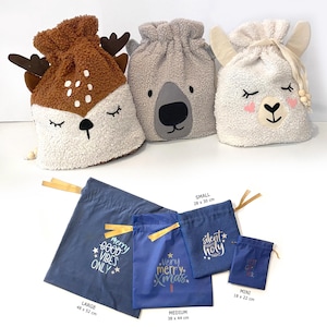 Può includere: Una collezione di sacchetti regalo con coulisse in varie dimensioni e design. Tre sacchetti di peluche presentano facce di animali: un cervo, un koala e un lama. Ulteriori sacchetti blu presentano testi a tema festivo, tra cui "Merry Good Vibes Only" e "Very Merry Xmas."