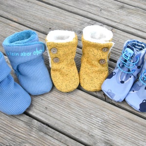 May include: Three pairs of baby booties in blue and yellow. The blue booties have different designs, one with a fold-over cuff and the text "klein aber oho", one with a lace-up design, and one with a fold-over cuff. The yellow booties have a button closure.