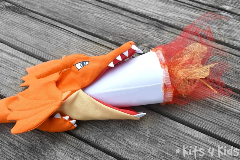 May include: Orange dragon puppet with a white cone in its mouth. The cone is decorated with red and gold tulle.