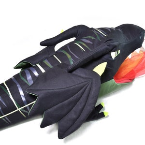 May include: A black and green plush dragon with a red and orange fabric flame coming out of its mouth. The dragon has wings and a long tail.