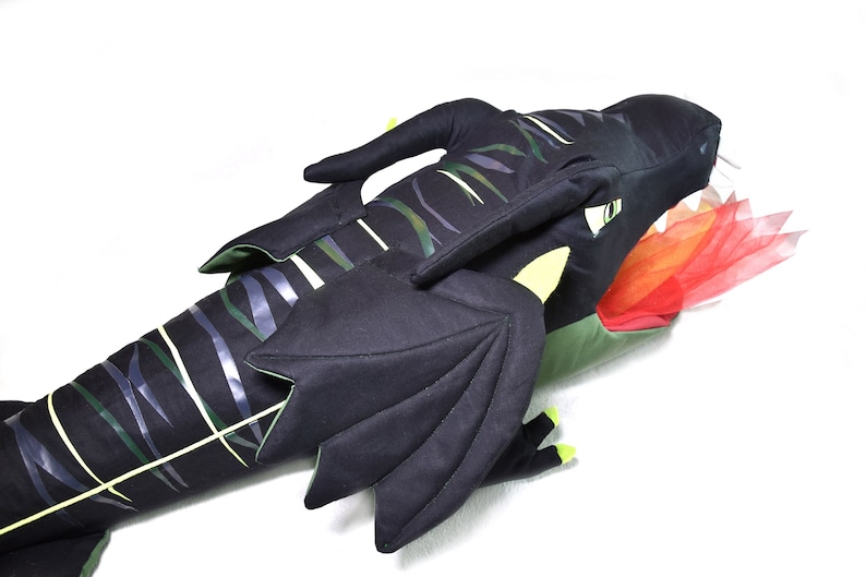 May include: A black and green plush dragon with a red and orange fabric flame coming out of its mouth. The dragon has wings and a long tail.