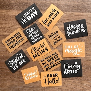 Może przedstawiać: Kolekcja prostokątnych drewnianych tabliczek z różnymi frazami w białym i czarnym tekście. Frazy to "Happy Day", "Classy & Fabulous" i "Full of Magic". Tabliczki ułożone są na drewnianej powierzchni.