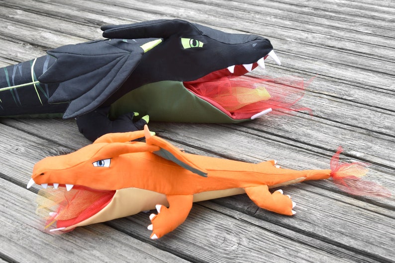 May include: Two plush dragon toys with open mouths and red mesh inside. The larger dragon is black with green accents and the smaller dragon is orange.