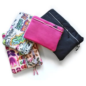Könnte beinhalten: Eine Sammlung von Reißverschlusstaschen in verschiedenen Farben und Mustern. Eine Tasche ist pink, eine andere schwarz mit dem Wort "online", und andere haben Blumen- und Graffiti-Designs. Jede Tasche hat einen Reißverschluss.
