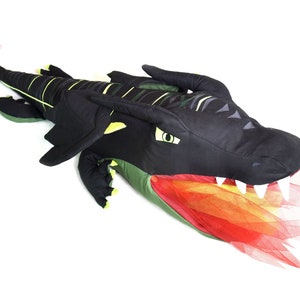 May include: A black and green plush dragon with a red and orange tulle tail. The dragon has a large head with yellow eyes and sharp teeth.
