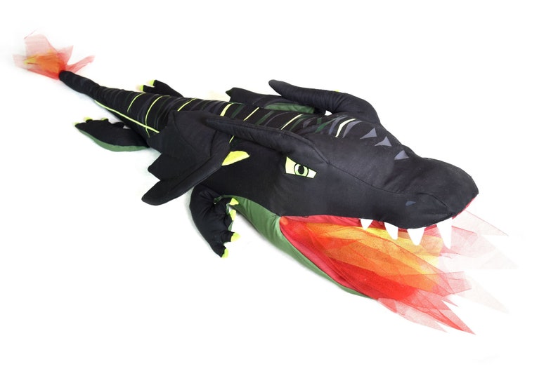 May include: A black and green plush dragon with a red and orange tulle tail. The dragon has a large head with yellow eyes and sharp teeth.