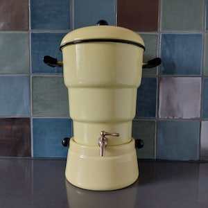May include: A yellow enamel coffee pot with a black lid and a brass spigot. The pot has a rounded base and a cylindrical body.