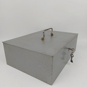 Puede incluir: Una caja de seguridad de metal gris con una manija plateada y una llave unida a la cerradura.