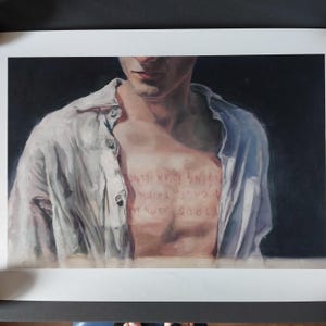 Op de afbeelding: Een afdruk van een schilderij met een persoon in een wit overhemd, met de tekst "BIRDS BORN IN A CAGE THINK FLYING IS AN ILLNESS" op hun borst. Het kunstwerk heeft een donkere achtergrond en richt zich op het bovenlichaam.