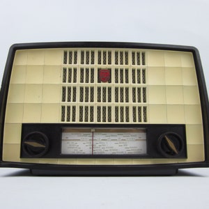 May include: A vintage black and cream radio with a speaker grille and a dial with station names and frequencies. The radio has two knobs on the front.
