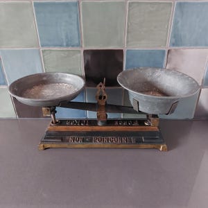 May include: Antique brass and black balance scale with two metal bowls. The scale has a wooden base with the words "POIDS" and "TOIXES" printed on it. The scale also has the words "NON POINCONNEE" printed on it.