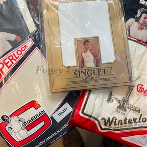 May include: An assortment of white undershirts packaged in plastic bags. The packaging features various brand names, including "Superlock", "Guardian", "Singlet", "Winterlock", and "Cross".