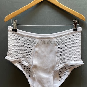 Puede incluir: Ropa interior blanca con diseño de malla en los laterales y panel frontal liso. El texto "Honey Unlimited" está impreso en la parte delantera. Colgada de una percha de madera.