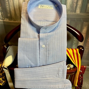 May include: A light blue dress shirt with a mandarin collar and double cuffs. The shirt has a subtle striped pattern and a label that reads "Foggy Unlimited, Home of the Elegant Gentleman".
