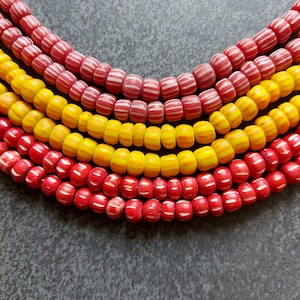 Può includere: Primo piano di diversi fili di perline colorate. Le perline sono rosse e gialle, alcune con strisce bianche. Le perline sono disposte in file curve, creando un motivo visivamente accattivante. Le perline sono probabilmente per la creazione di gioielli.