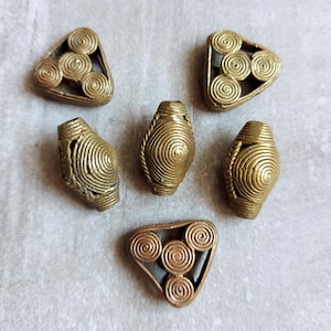 May include: A collection of six antique brass beads. The beads are in various shapes, including triangles and ovals, and feature a spiral design. The brass has a warm, aged patina. These beads are suitable for jewelry making and craft projects.