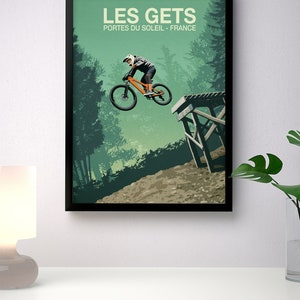 May include: A vintage-style poster with a green background featuring a mountain biker in mid-air, jumping over a wooden ramp. The poster has the text "LES GETS" in large white letters and "PORTES DU SOLEIL - FRANCE" in smaller white letters.