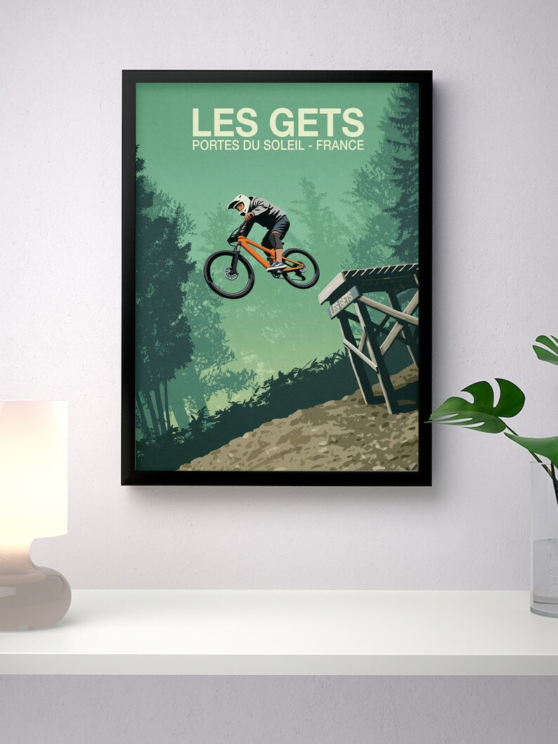 May include: A vintage-style poster with a green background featuring a mountain biker in mid-air, jumping over a wooden ramp. The poster has the text "LES GETS" in large white letters and "PORTES DU SOLEIL - FRANCE" in smaller white letters.