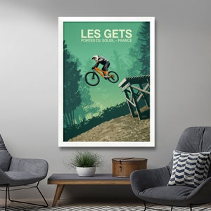 May include: A vintage-style poster with a green background featuring a mountain biker in mid-air, performing a trick over a wooden ramp. The poster has the text "LES GETS" in white lettering, with the words "PORTES DU SOLEIL - FRANCE" in smaller white lettering below.