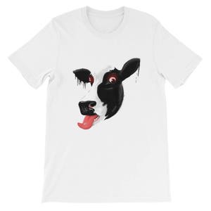 May include: White t-shirt featuring a black and white cow face graphic. The cow has red eyes and is sticking its tongue out.