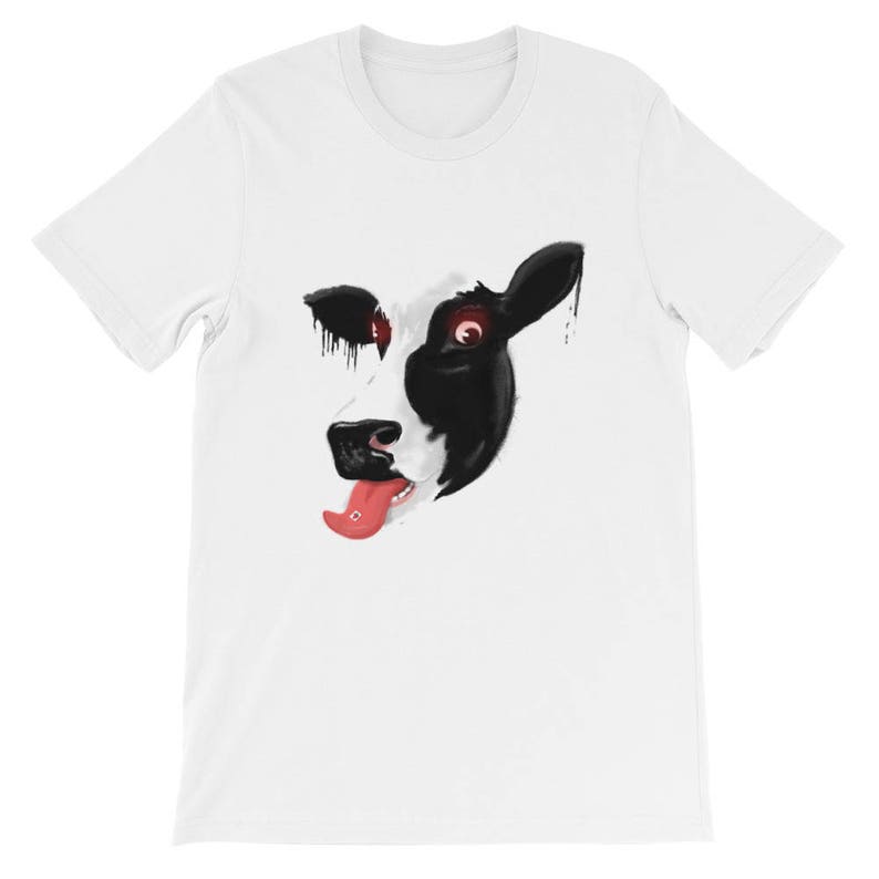 May include: White t-shirt featuring a black and white cow face graphic. The cow has red eyes and is sticking its tongue out.