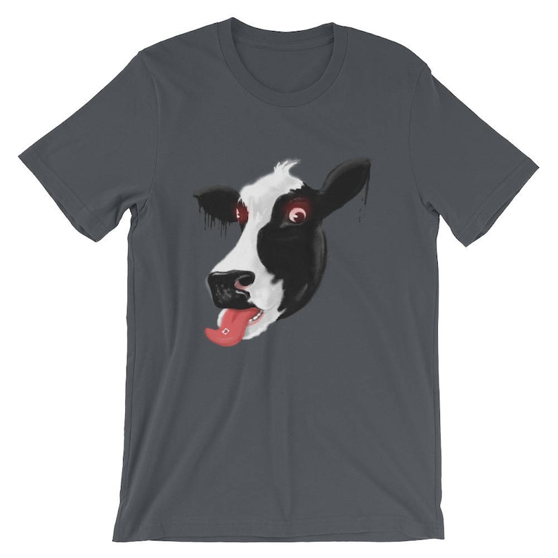 May include: A dark grey t-shirt featuring a graphic of a cow's face with red eyes and a pink tongue sticking out. The cow's face is partially obscured by the shirt's neckline.