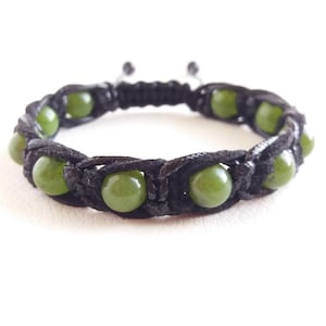 May include: A black cord bracelet with green jade beads. The bracelet is knotted and has a sliding closure.