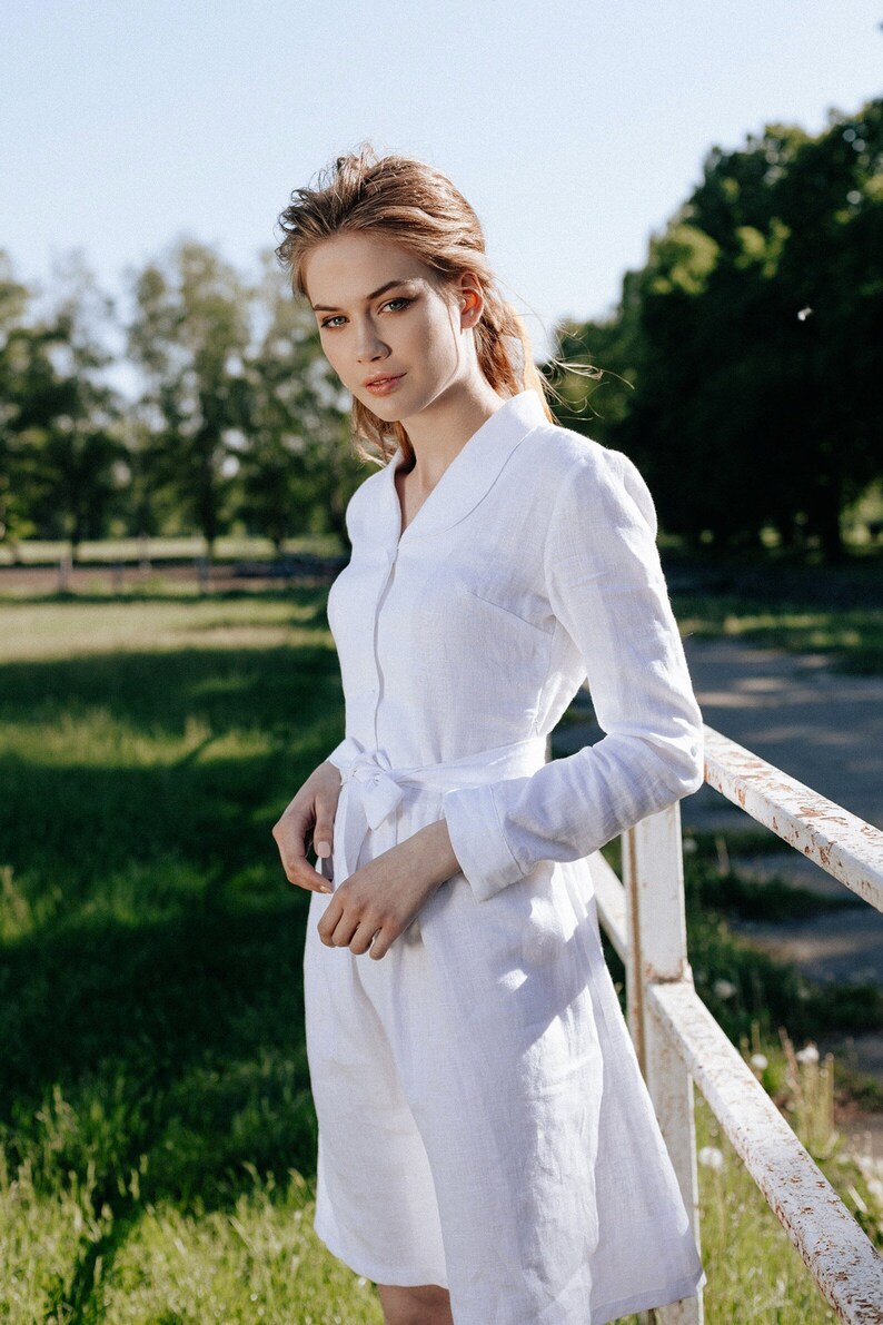 a woman in a white dress leaning against a fence