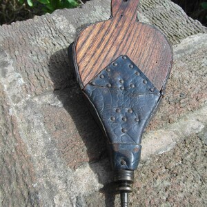 May include: A wooden and leather bellows with a brass nozzle. The bellows is brown with a dark blue leather panel and metal rivets.