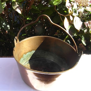 May include: A vintage brass bucket with a handle. The bucket has a worn, aged patina and is perfect for rustic decor.
