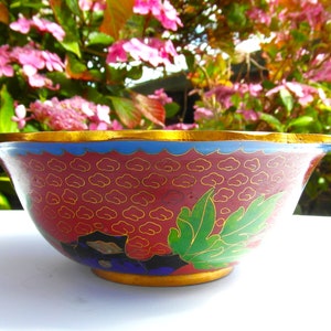 May include: A red and gold cloisonn&eacute; bowl with a floral design. The bowl has a scalloped rim and is decorated with green leaves and gold clouds.
