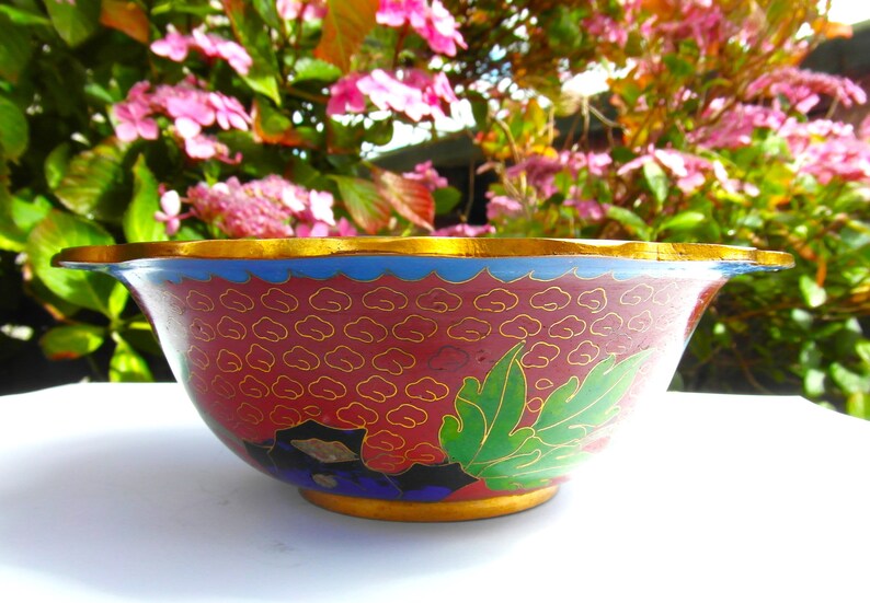 May include: A red and gold cloisonn&eacute; bowl with a floral design. The bowl has a scalloped rim and is decorated with green leaves and gold clouds.