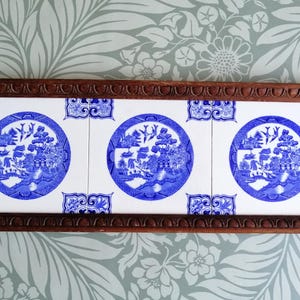 May include: A rectangular serving tray with a dark brown wooden frame and brass handles. The tray has three white tiles with blue, circular landscape designs. A decorative item.