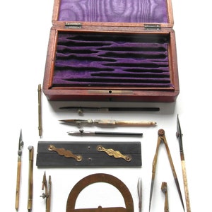 May include: A wooden box with a purple velvet lining, containing a set of vintage drafting tools. The tools include a compass, protractor, ruler, and various drawing implements.