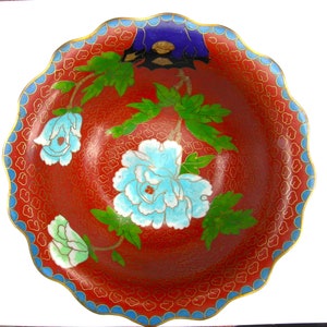 May include: A red and blue cloisonn&eacute; bowl with a scalloped rim. The bowl is decorated with a floral design featuring white, blue, and green flowers.