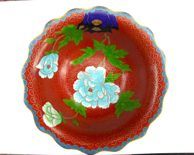 May include: A red and blue cloisonn&eacute; bowl with a scalloped rim. The bowl is decorated with a floral design featuring white, blue, and green flowers.
