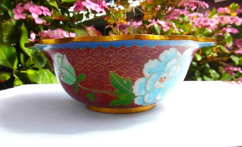 May include: A red and blue cloisonn&eacute; bowl with a floral design. The bowl has a scalloped rim and a gold trim.