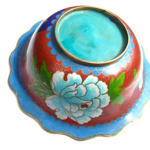 May include: A small, round, blue and red cloisonn&eacute; bowl with a floral design. The bowl has a scalloped edge and a turquoise blue interior.