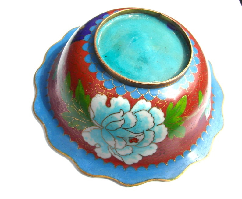 May include: A small, round, blue and red cloisonn&eacute; bowl with a floral design. The bowl has a scalloped edge and a turquoise blue interior.